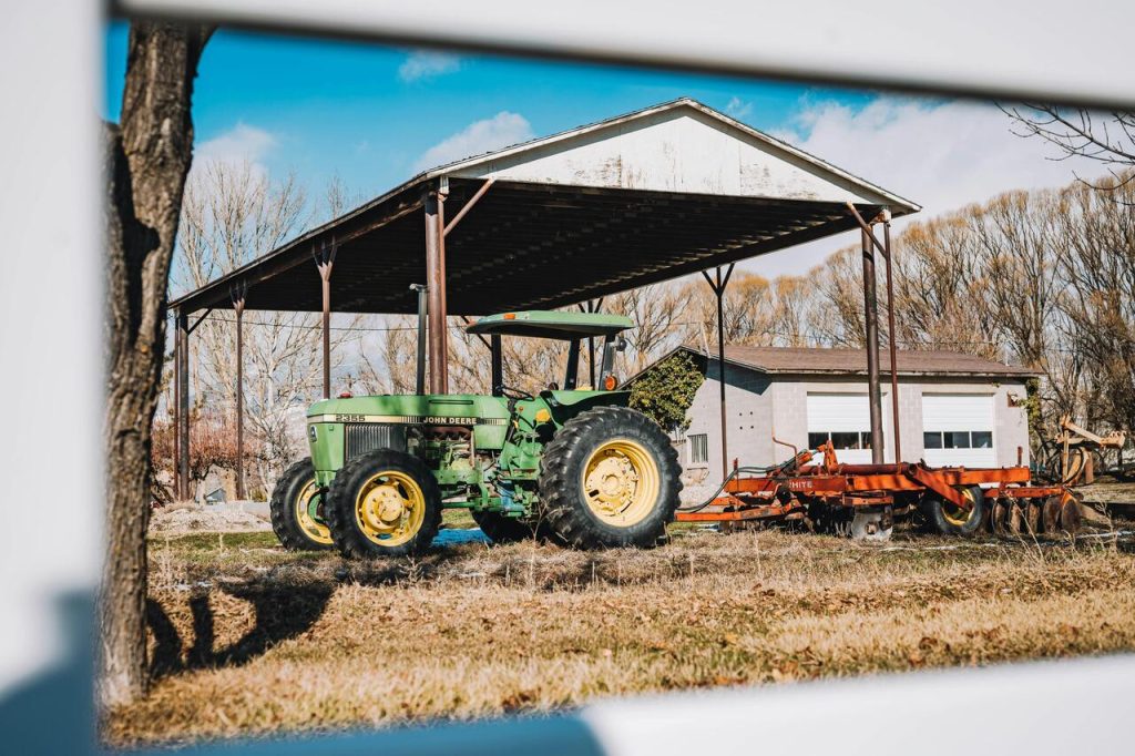 Zeleni traktor sa tanjirastim priključkom ispod otvorenog natkrivenog skloništa