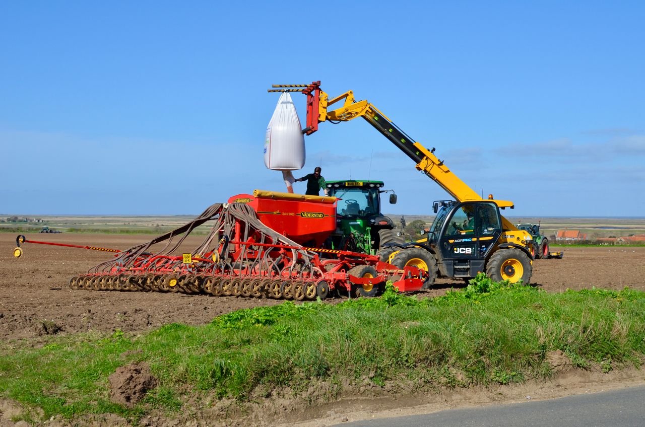 Utovarivač sipa seme iz vreće u sejalicu priključenu za traktor na njivi.